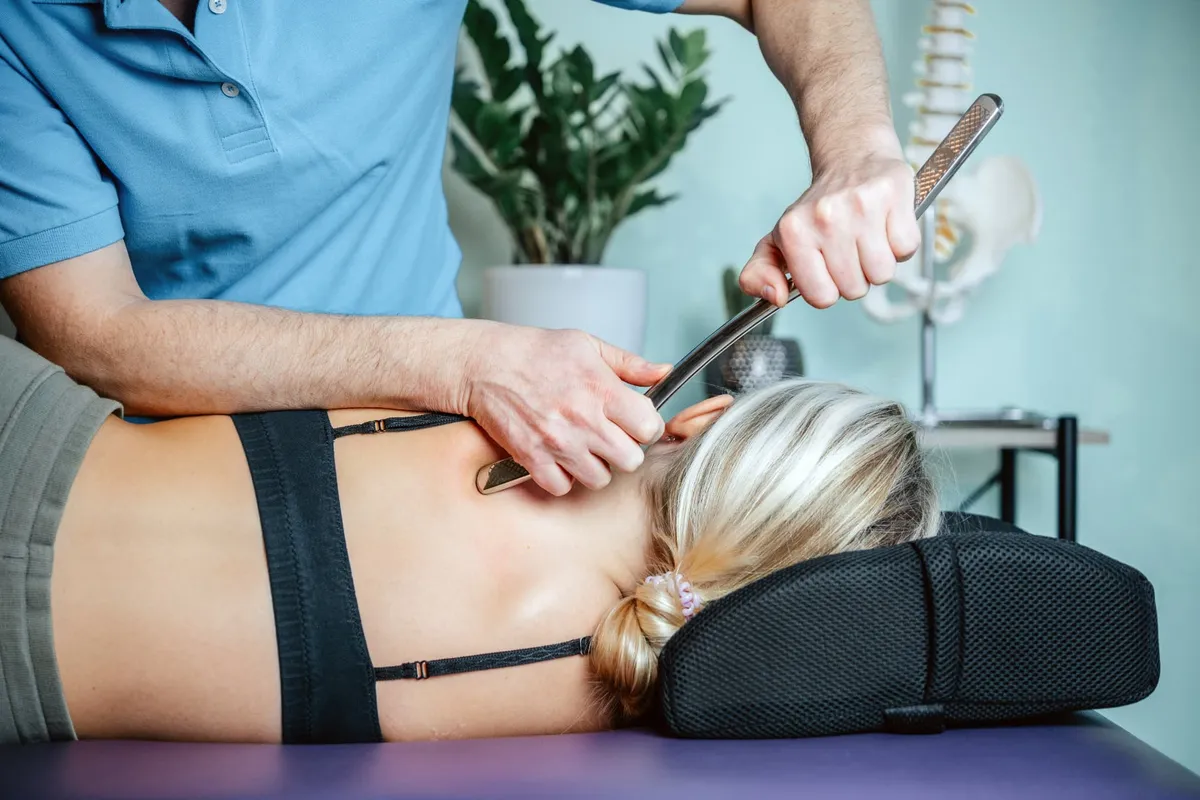 A clinician using an instrument-assisted soft-tissue technique along a patient’s upper back