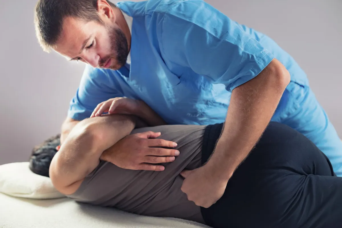 A chiropractor performing a gentle side-lying adjustment for a patient on a treatment table