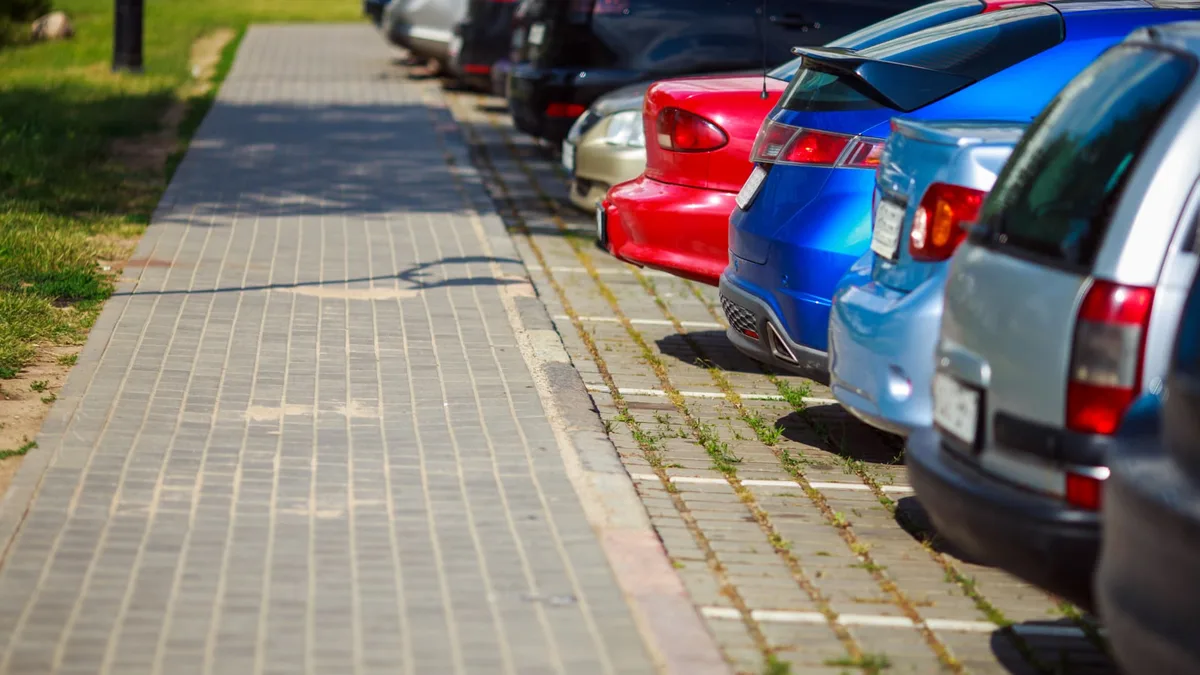 Cars parked in a row on a paved lot beside a brick walkway