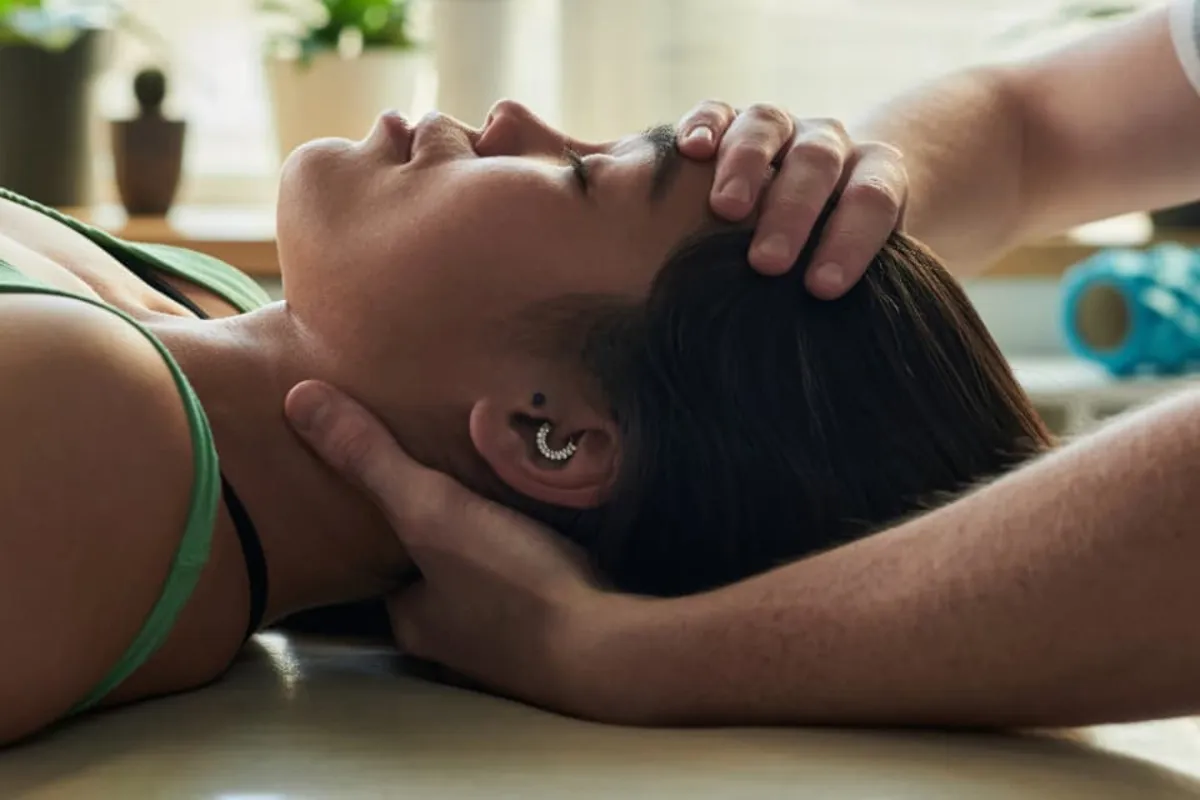 A clinician performing gentle upper-neck care for a patient lying face-up on a treatment table