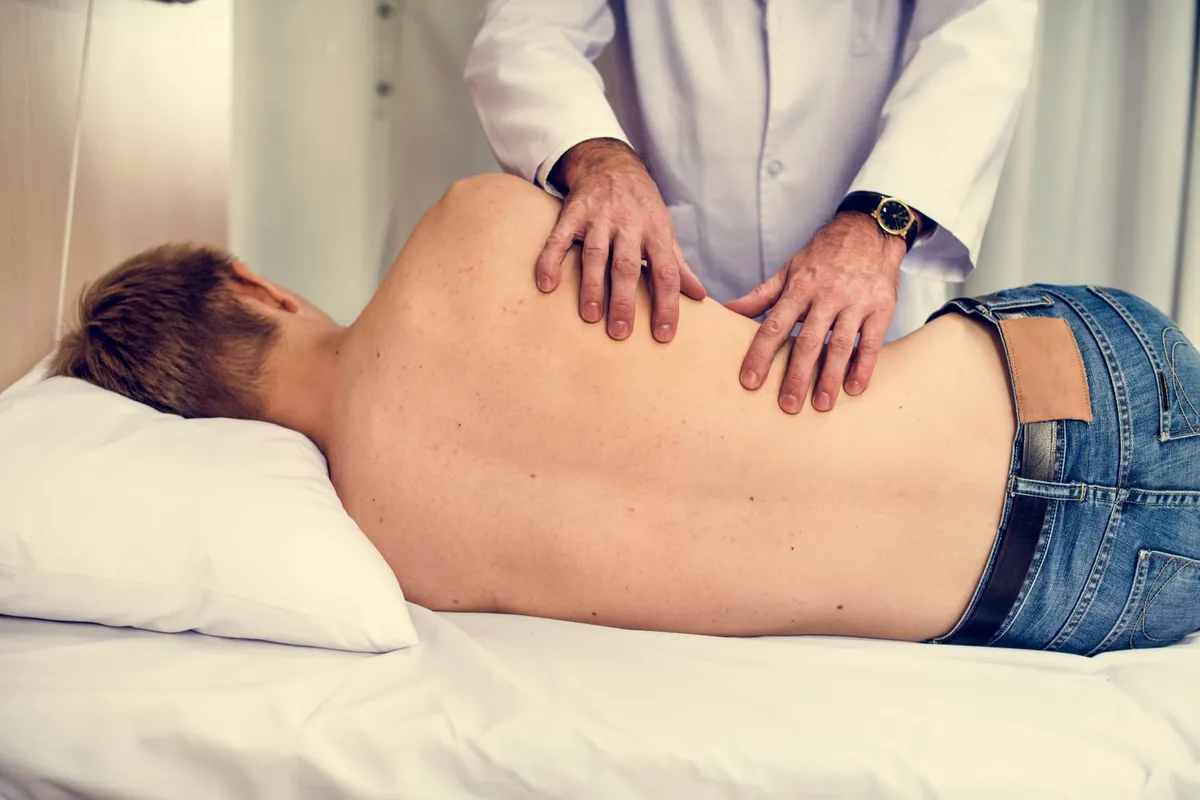 A chiropractor using gentle hands-on pressure along a patient’s mid-back during a treatment visit
