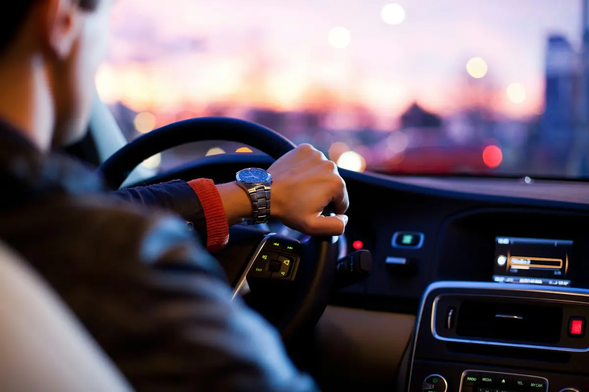 A driver holding the steering wheel on a city road at dusk